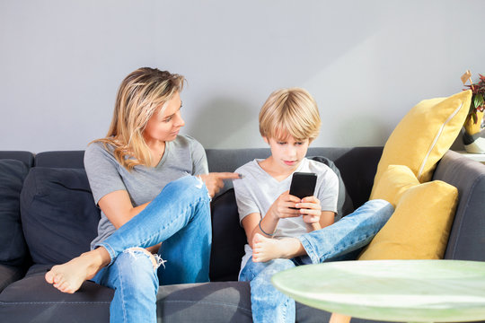 Beautiful woman is scolding her teenage son, boy is playing video games on smartphone and ignoring his mom.Childhood, technology and family concept