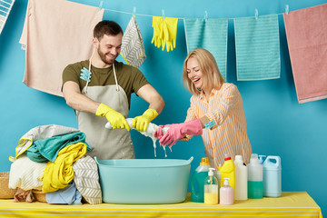 positive man and blonde woman enjoing sqeezing process in the laundry roo. husband helps his wife to do washing. clean clothes hanging on the clothesline in the backgrond of the photo