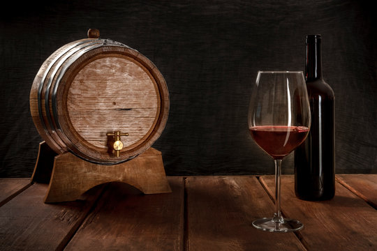 A Glass Of Wine With A Bottle And A Wine Barrel, Side View On A Dark Rustic Background, Low Key Photo With A Place For Text