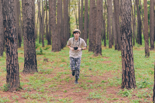 Asia man wears shirt, hat, and camouflage pants are running and taking photos at the forest.
