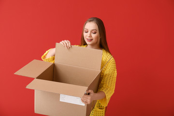 Young woman with open cardboard box on color background