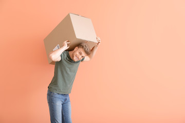 Young man with heavy cardboard box on color background