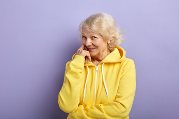 Optimistic elder female coach or trainer dressed in light sports suit and headband posing in studio on blue background, copyspace
