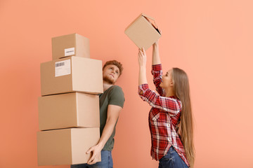 Young couple with many cardboard boxes on color background