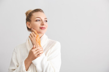 Young woman applying body scrub against light background