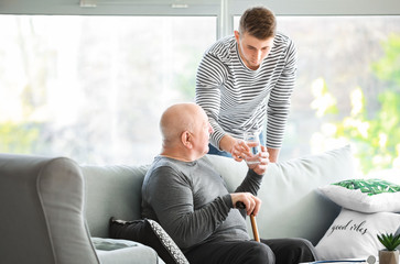 Male caregiver giving glass of water to senior man in nursing home - Powered by Adobe