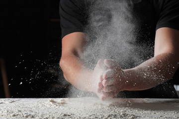 Fototapeta na wymiar Man clapping hands in flour on dark background