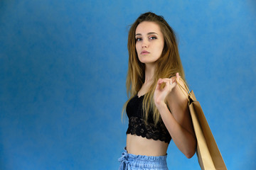 Photograph of a portrait of a beautiful girl woman with long dark flowing hair, loves shopping, on a blue background with packages from the store. She is standing in different poses and smiling.