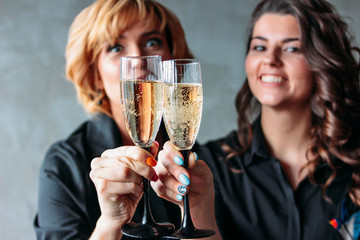 Two beautiful girls in black dresses celebrate the event with champagne. Friendship, corporate, successful female business