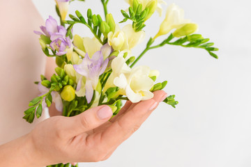Woman with beautiful freesia flowers on light background, closeup