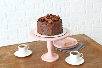 Stand with tasty chocolate cake and cups of coffee on table