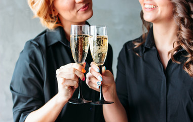 Two beautiful girls in black dresses celebrate the event with champagne. Friendship, corporate, successful female business