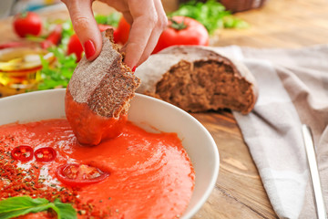 Woman dipping bread into bowl with tasty cream soup, closeup