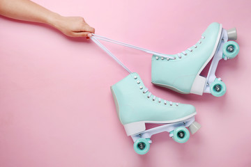 Female hand and vintage roller skates on color background