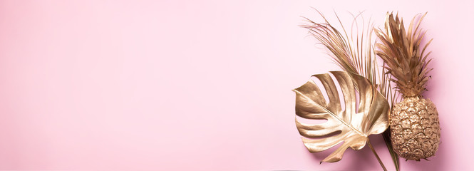 Creative layout. Gold pineapple and golden palm, monstera on pink background with copy space. Top view. Tropical flat lay. Exotic food concept, crazy trend. Banner
