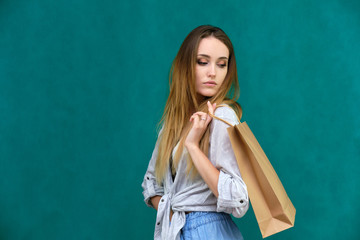 Photograph of a portrait of a beautiful girl woman with long dark flowing hair, loves shopping, on a green background with packages from the store. She is standing in different poses and smiling.