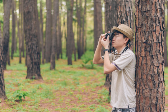 Asia man wears shirt, and hat are stand against the tree and taking photos at the forest.