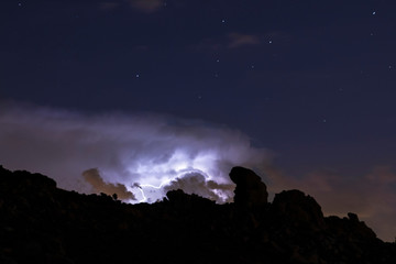 Rays and clouds in night storm over the mountain under a starry sky