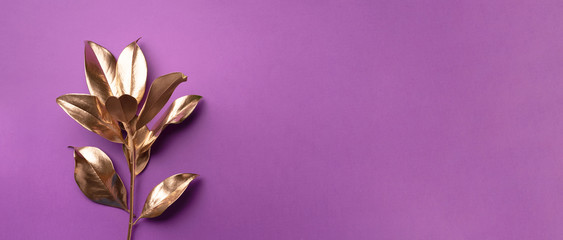 Floral minimal style concept. Exotic summer trend. Golden tropical leaves and branch on violet color background. Shiny and sparkle design, fashion concept.