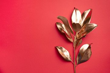 Floral minimal style concept. Exotic summer trend. Golden tropical leaves and branch on red color background. Shiny and sparkle design, fashion concept.
