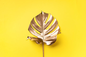 Golden tropical monstera leaf on yellow background with copy space. Top view. Flat lay. Creative layout. Exotic summer concept in minimal style