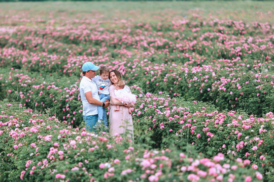 Beautiful and happy family, father, mother, son and cute little daughter are walking in a lush rose garden over yellow magic sunset lights.