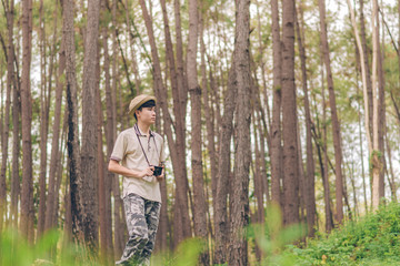 Naklejka premium Asia man wears shirt, hat, and camouflage pants are walking and taking photos at the forest.
