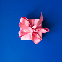Fototapeta premium Pink gift box with a pink ribbon on a blue background . Holiday concept. Copy space. Flat lay.
