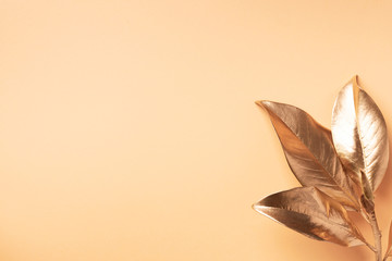 Floral minimal style concept. Exotic summer trend. Golden tropical leaves and branch on pastel nude color background. Shiny and sparkle design, fashion concept.