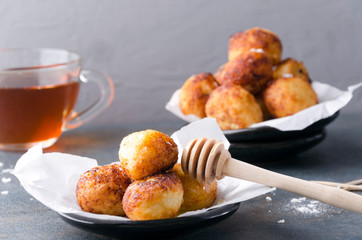 Fresh cooked cheese balls with honey and powdered sugar.Closeup of sweet donut holes with cup of tea and honey