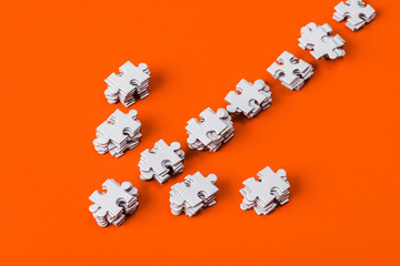 top view of direction arrow with white jigsaw puzzle pieces on orange
