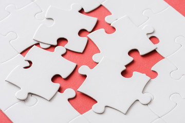 Fototapeta premium unfinished jigsaw near connected white puzzle pieces on red