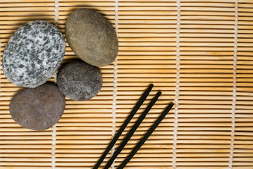 Stones lie on a bamboo rug next to fragrant chopsticks. Spa, relaxation, tranquility. Empty space for text