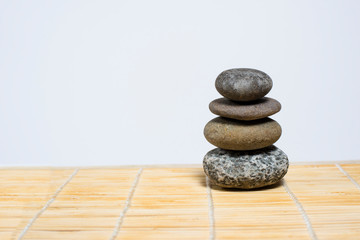 Stones stand on top of each other on a bamboo mat on a white background. Spa, relaxation, tranquility. Empty space for text