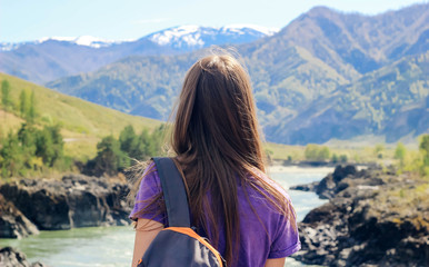 Young woman standing backwards and watching river in mountainous landscape. Girl with backpack on background of nature. Concept of tourism, travel