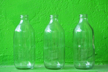 Empty recycle three glass bottles on green backgorund.
