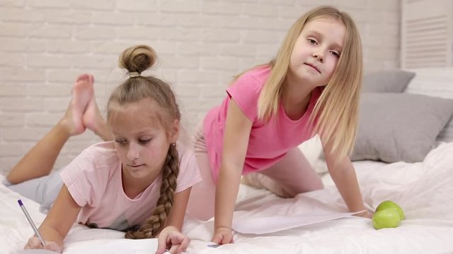 kids drawing pictures while lying on bed. pajama party and friendship.