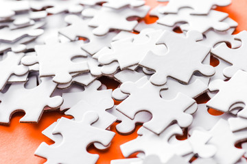 selective focus of incomplete white jigsaw puzzle pieces on orange