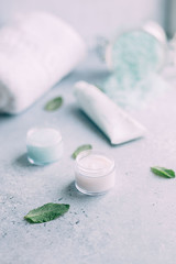 Obraz na płótnie Canvas pa and body care products. Blue scrub, white cream face sea salt, towel, mint on grey background. Beauty skin care. Spa treatment