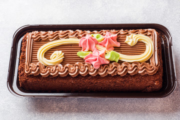 Chocolate rectangular cake decorated with cream roses on a light table. Sweet food is a...