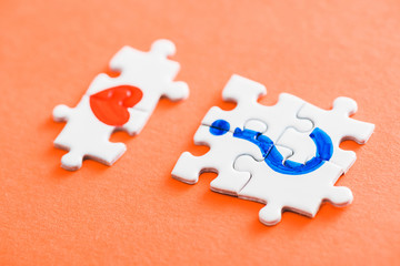 selective focus of connected puzzle pieces with drawn red heart and blue question mark on orange