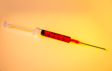 Syringe with blood on orange background