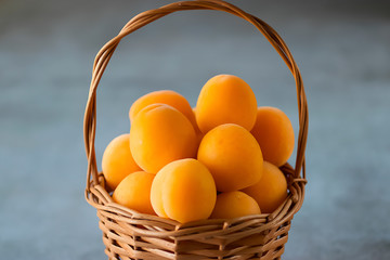 Ripe apricots to a brown basket on a gray background.