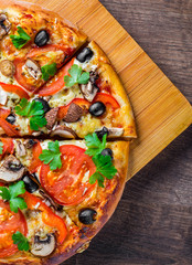 sliced Pizza with Mozzarella cheese, Tomatoes, pepper, olive, mushrooms, Spices and Fresh leaf. Italian pizza on wooden table background