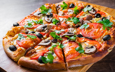 sliced Pizza with Mozzarella cheese, Tomatoes, pepper, olive, mushrooms, Spices and Fresh leaf. Italian pizza on wooden table background