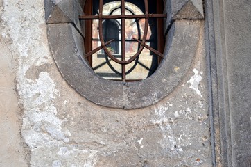 ancient wall with part of the oval window with the reflection of the building opposite and wrought iron bars on it