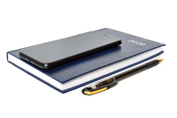 Closed blue leather notebook for new year with text 2020 on cover, ballpoint pen and black classic modern smartphone of front side on white background. Isolated