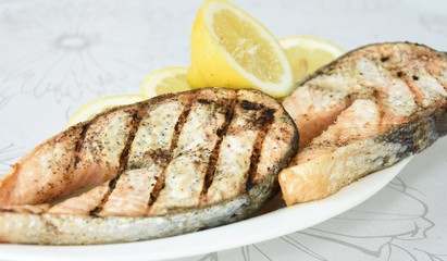 pieces of fish grilled salmon and lemon wedges on a white plate