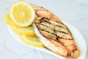 pieces of fish grilled salmon and lemon wedges on a white plate