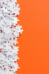 top view of unfinished white jigsaw puzzle pieces isolated on orange with copy space